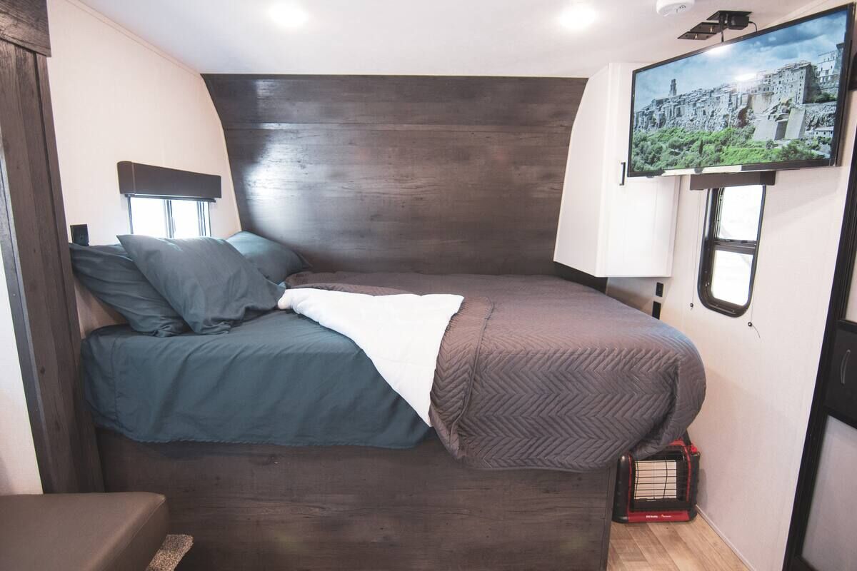 Bed with a wood headboard and wall-mounted TV in the Houston Camper
