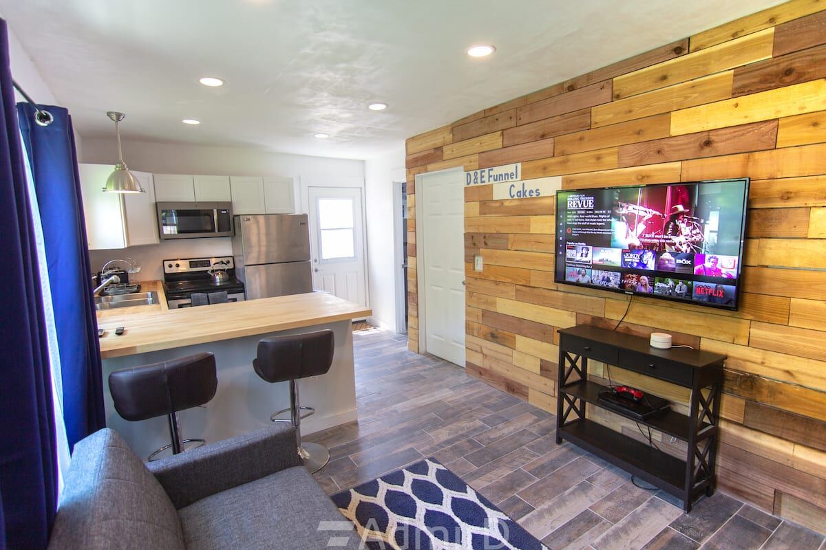 Open living area with a wood plank accent wall, TV and kitchen peninsula in the Corpus Christi guest house