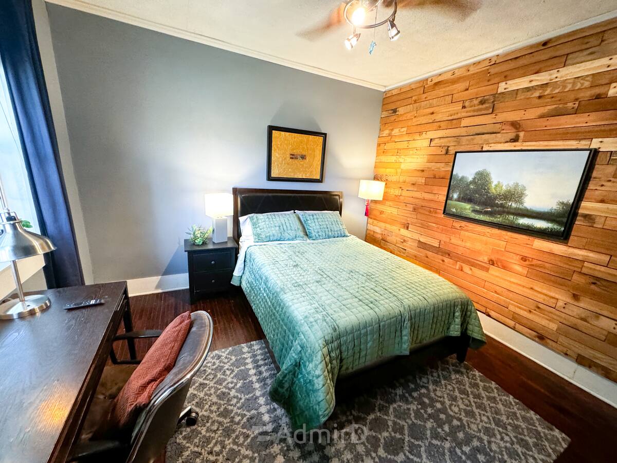 Furnished private bedroom with a queen bed, teal quilt and wood accent wall in a Midtown Houston home