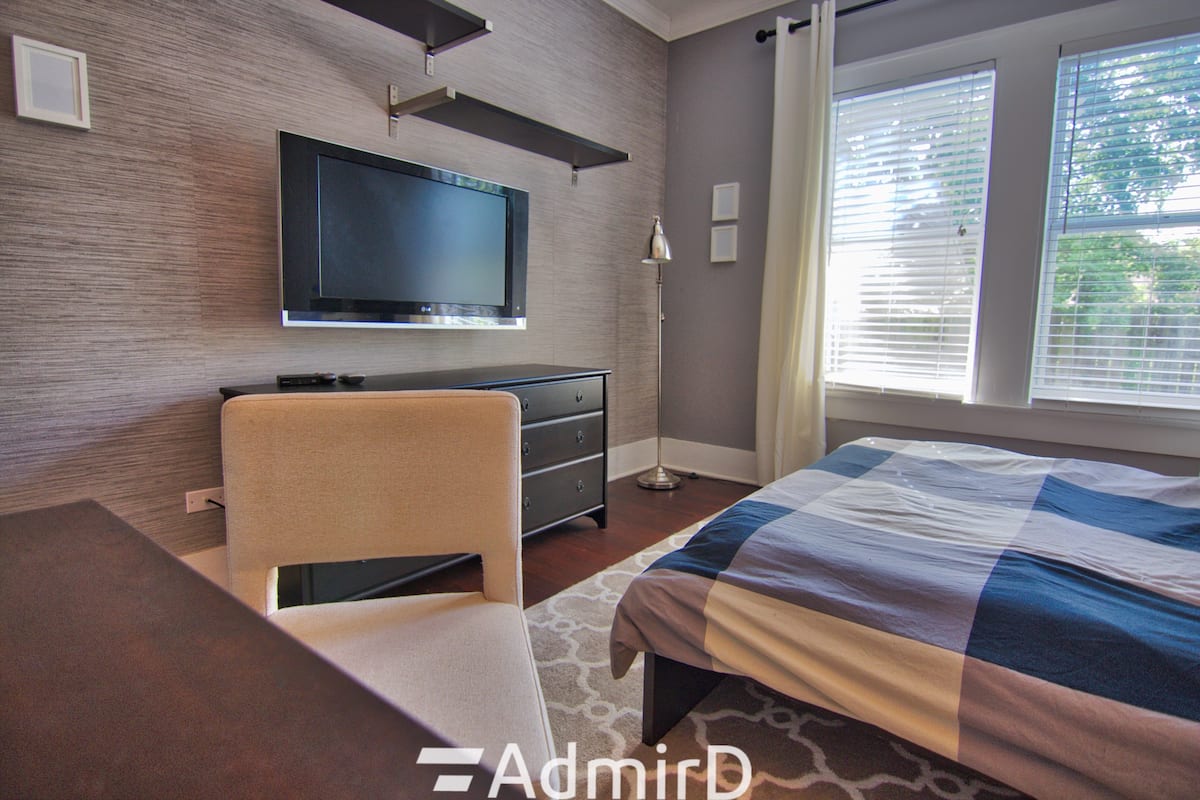 Room with a wall-mounted TV, dresser and chair beside two windows