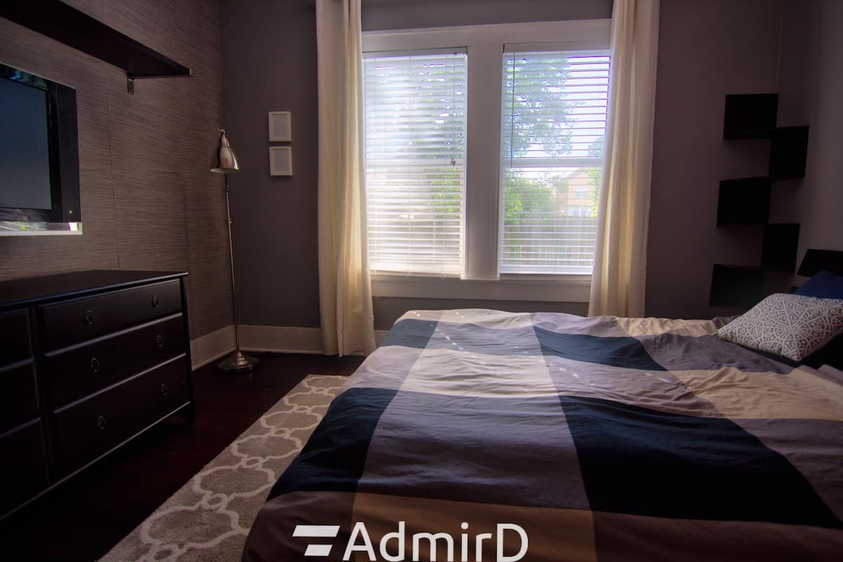 Room with a TV, dresser and tall windows with blinds